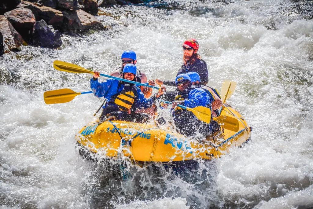A group of adventurers navigating turbulent white water rapids, splashing through waves and foam in Colorado.