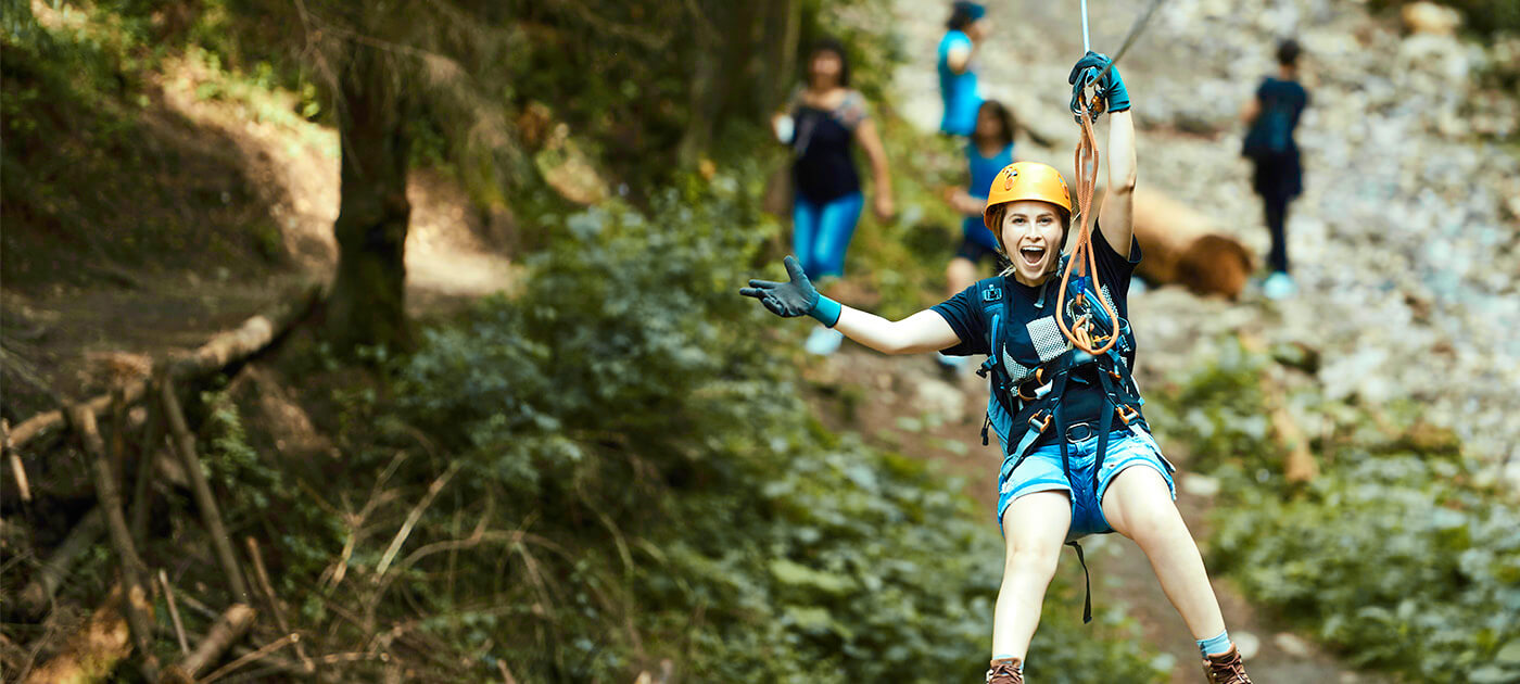 A woman ziplining with her right hand out in excitment