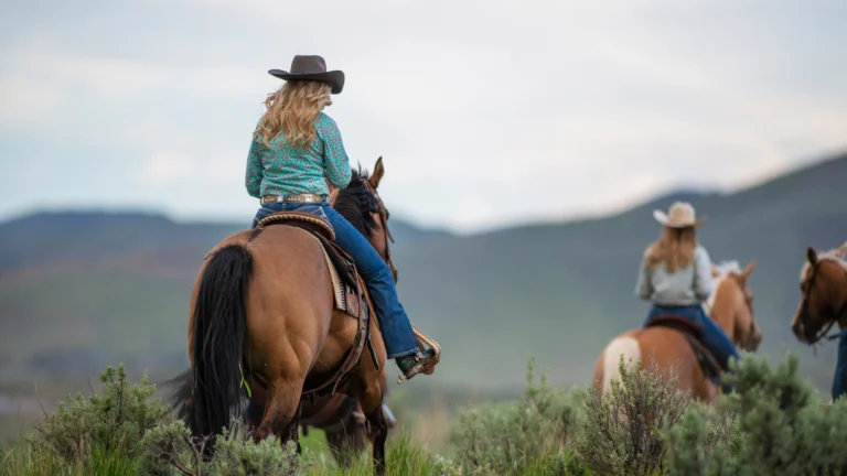 group horseback riding through green shrubbery and Colorado mountains