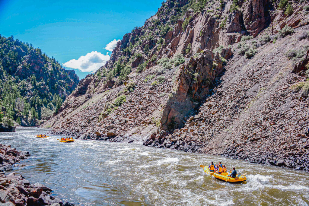 three rafts on the upper colorado river with rocky cliffs on either side.