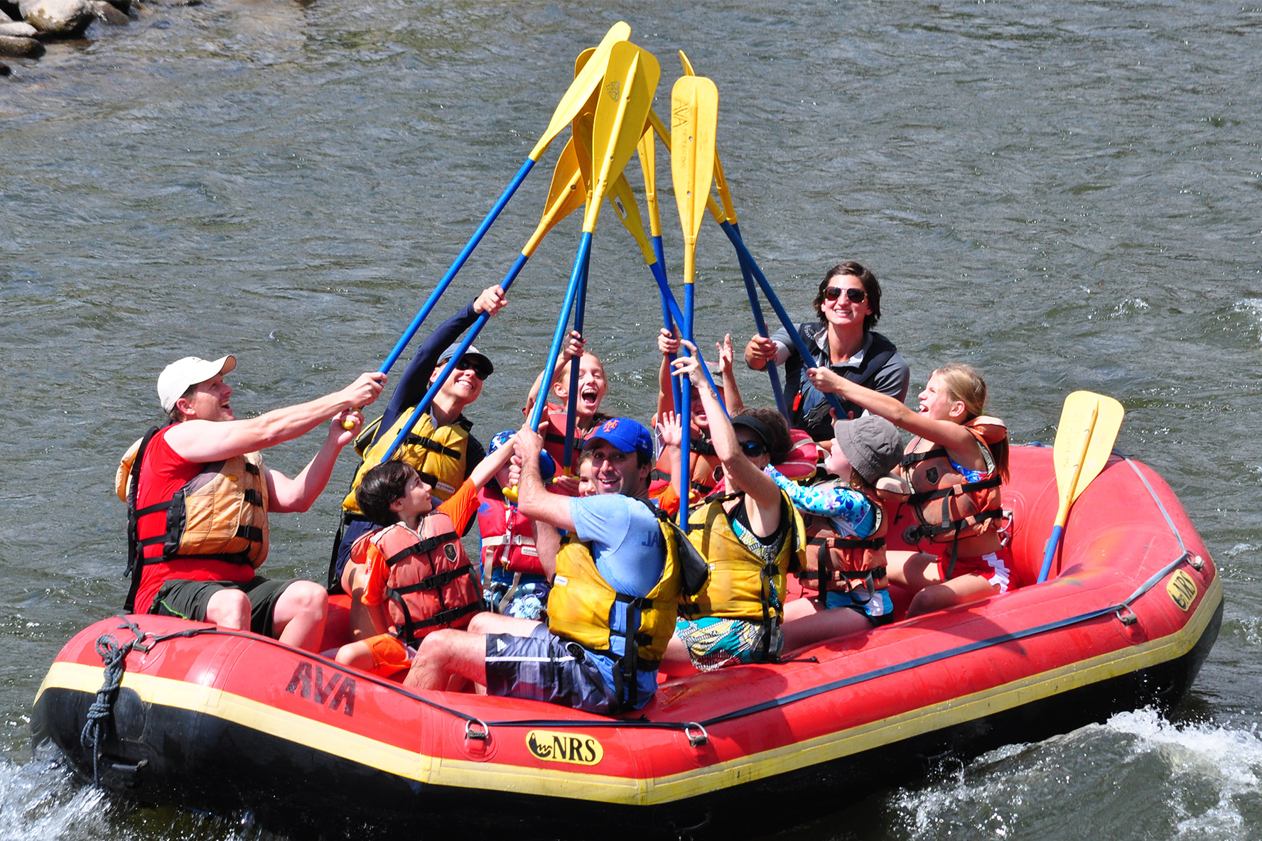 A group of rafters high fiving with the paddles while floating down the river