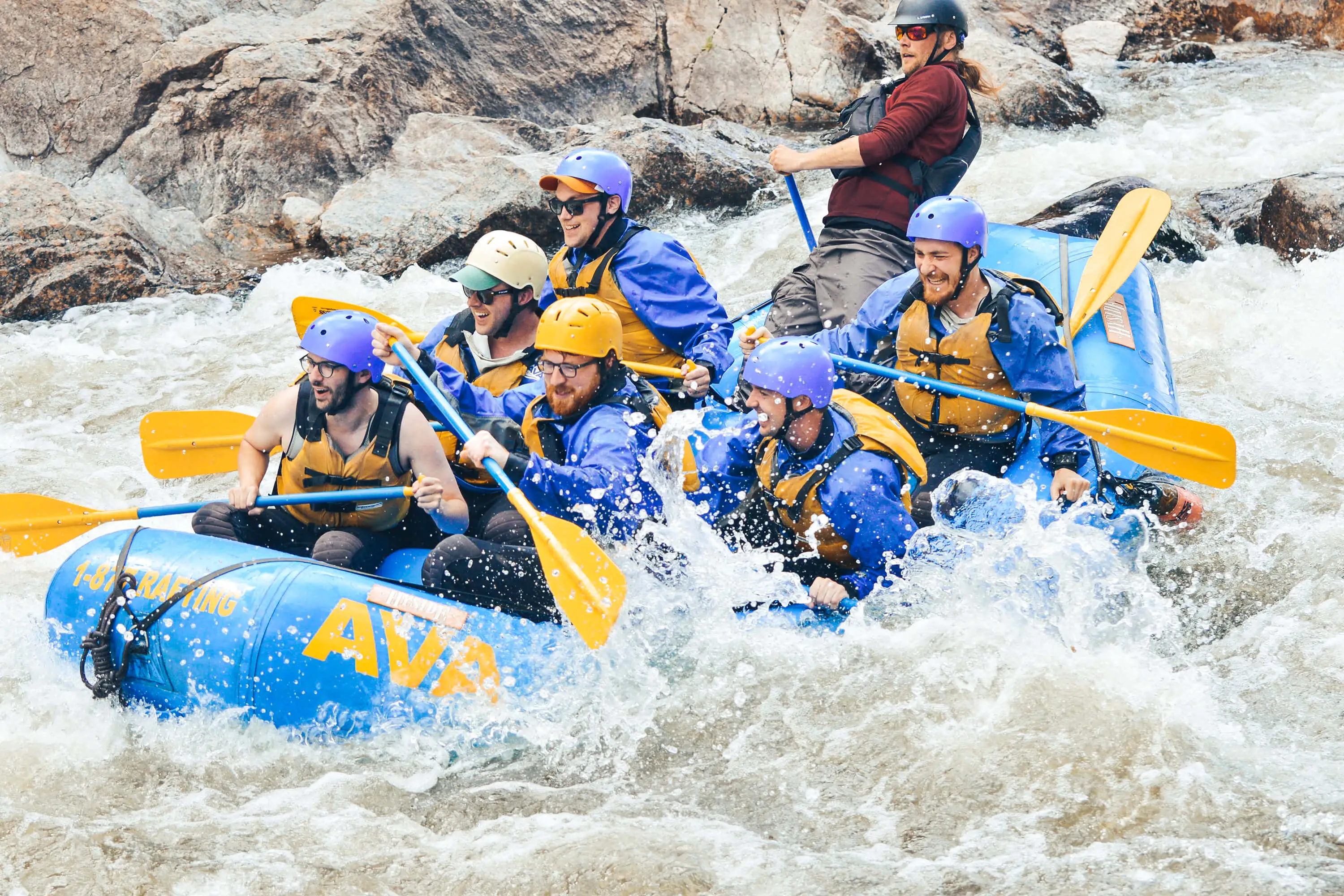 A group of men rafting through a whitewater rapid with smiles on their faces