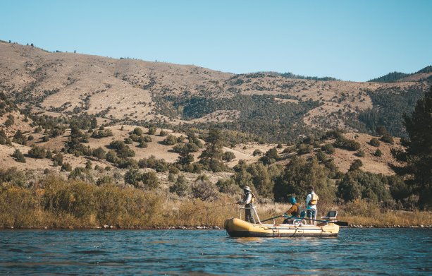 Three men on a fly fishing raft with a mountain in the background