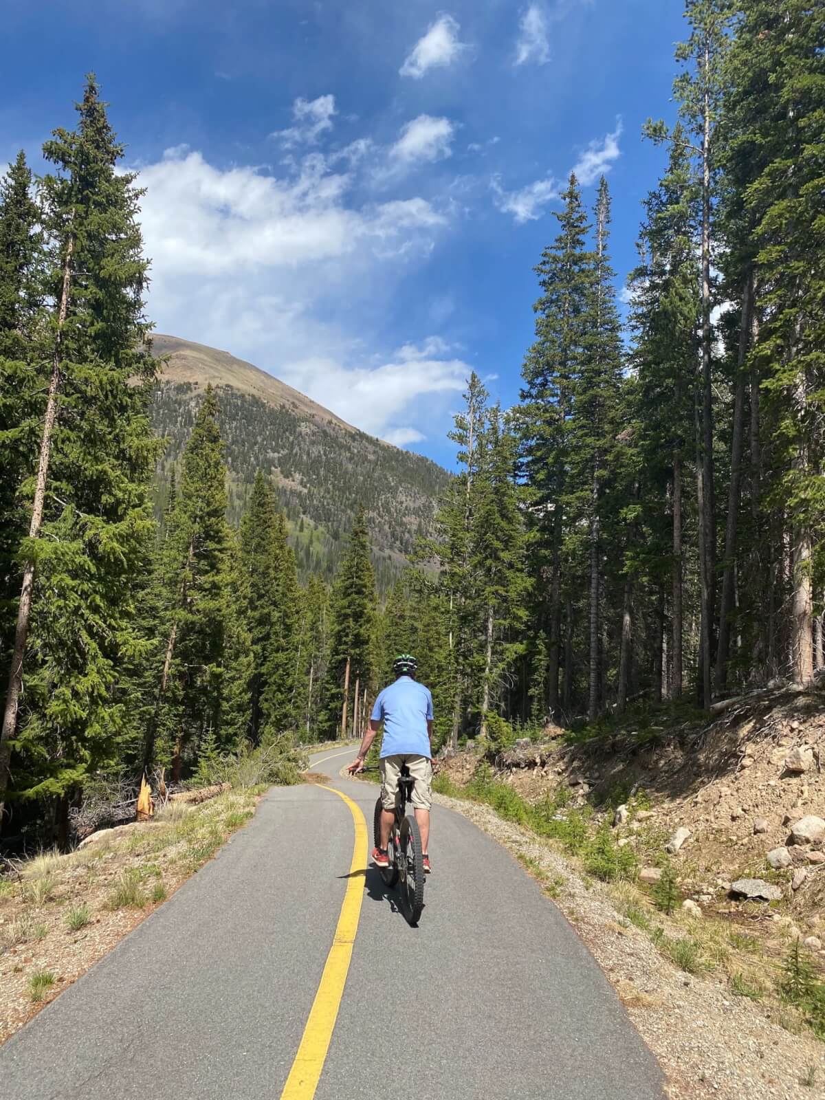 A man in a blue shirt biking on a path in Idaho Springs, Colorado during the summer