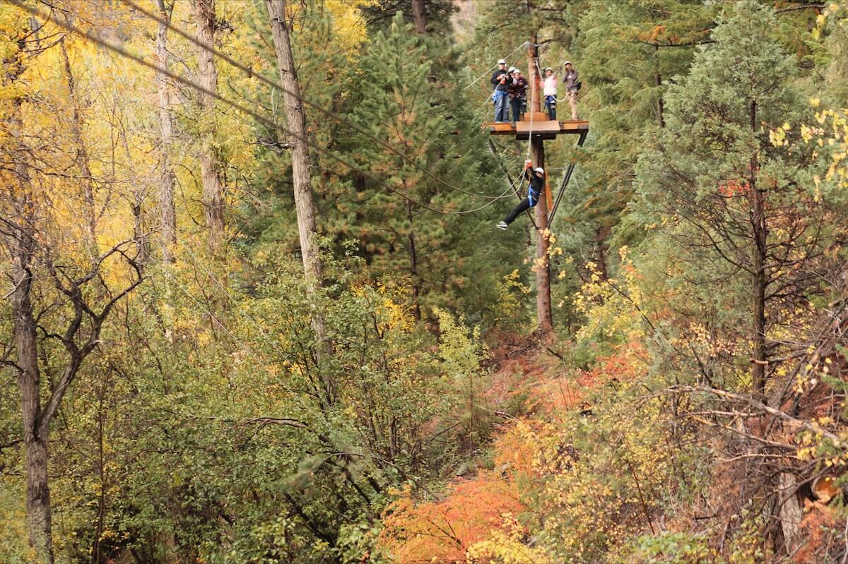 Woman ziplining over a river in the fall with orange, green, and yellow trees everywhere in Idaho Spings