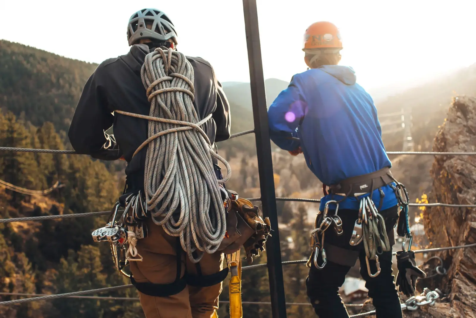 Two men looking at the valley below wearing via ferrata gear as the sun sets