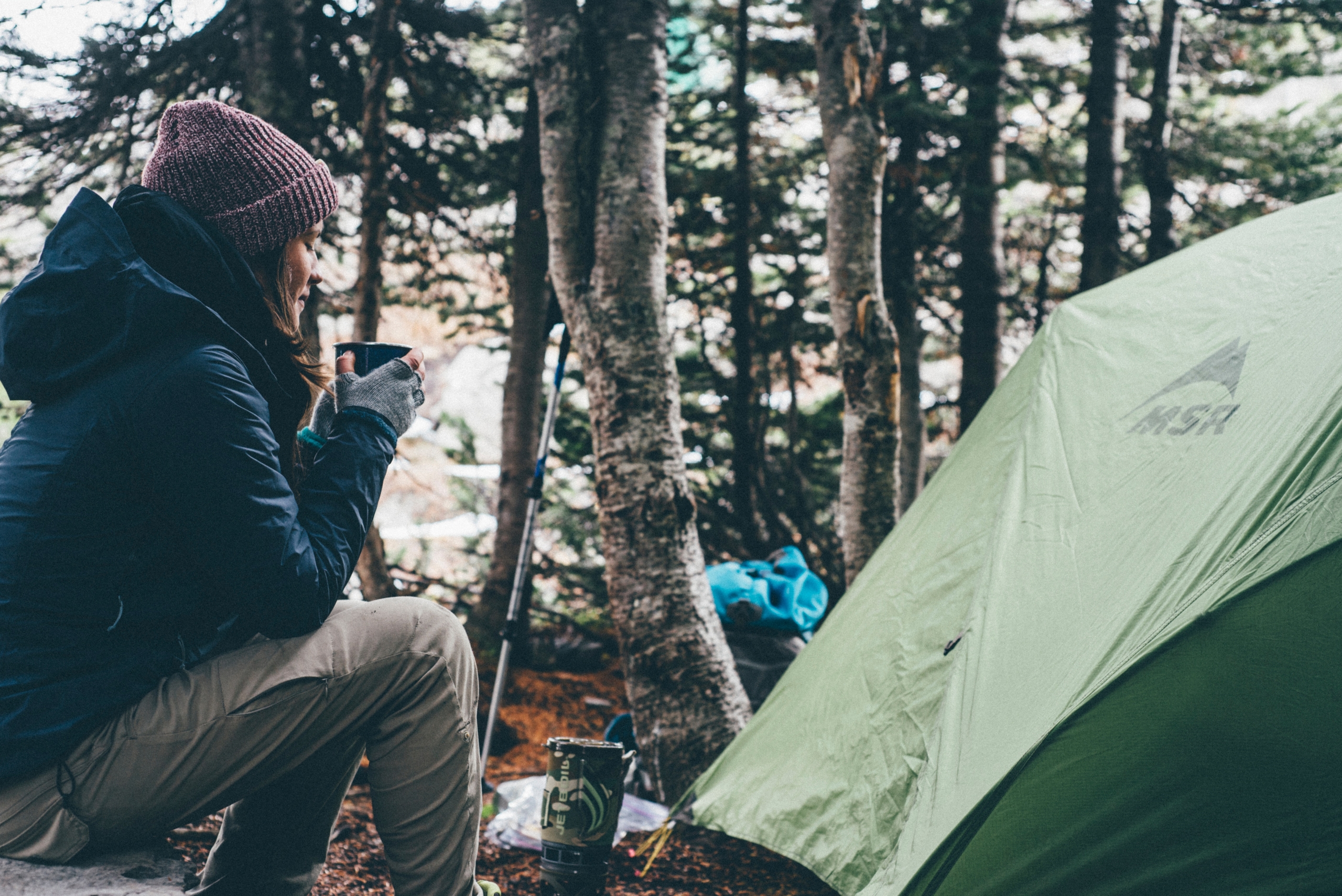 woman camping blowing on hot drink outside tent