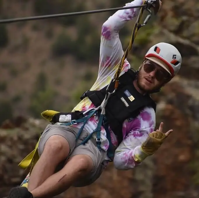 Man in sunglasses showing the peace sign with is fingers while ziplining