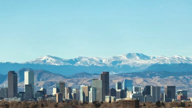 A view of the Denver Colorado city skyline with snow-capped mountains in the background pointed west.