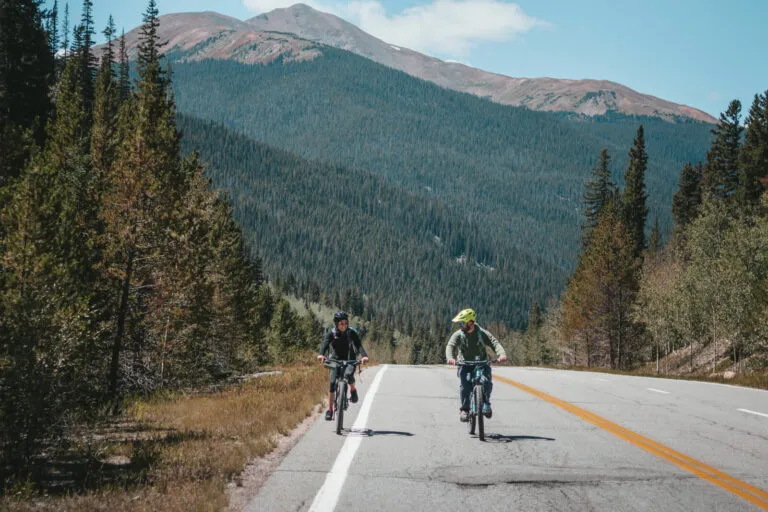 a man and woman biking on a road in Summit County with mountains in the background