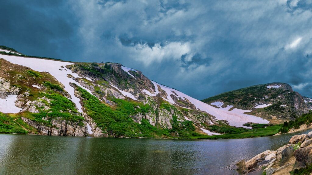 lake near Idaho Springs with snow and greenery on the sloped bank