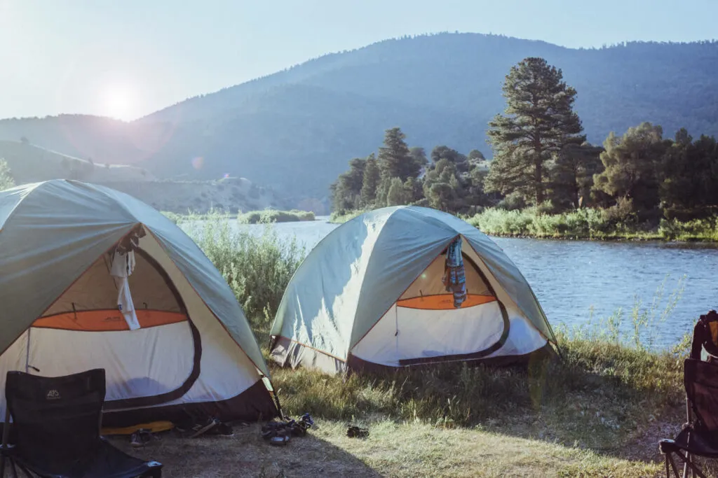 Two tents next to the river with the morning sun shining over the mountain in the background