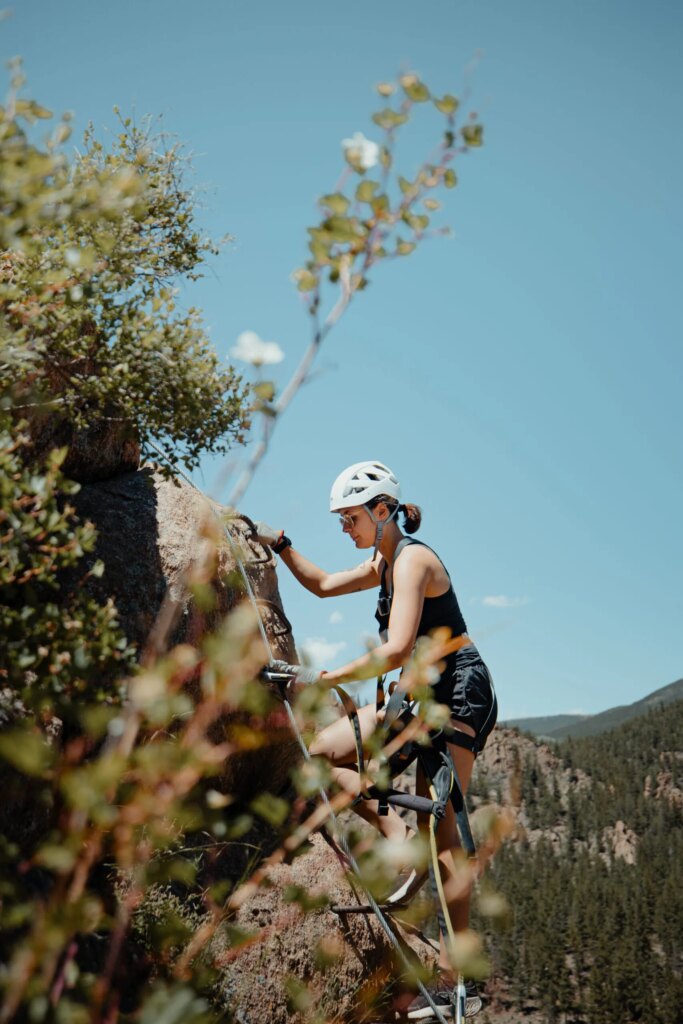 view of woman climbing Via Ferrata through trees and shrubbery