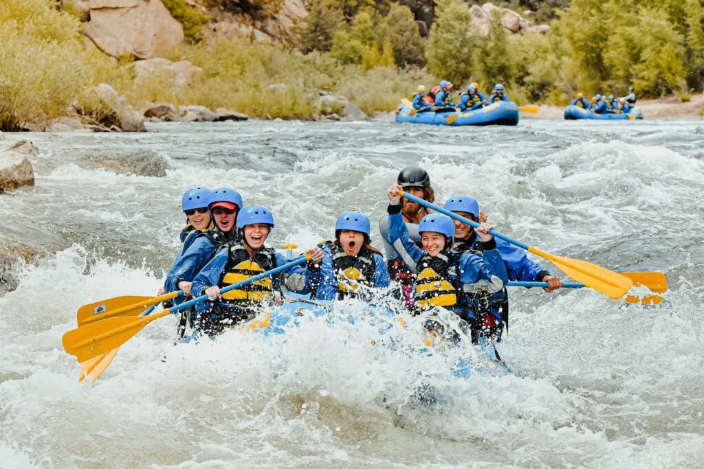 group smiling and laughing as their raft heads toward a big wave.