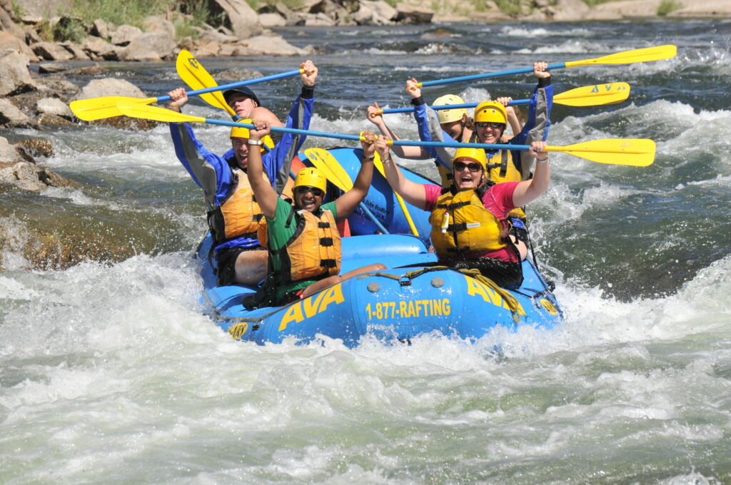 Group smiling and laughing while holding up their paddles in a raft